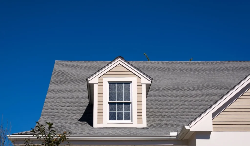 Professional shingle installation on a residential dormer against a clear blue sky, showcasing the clean lines and precision of The Roof Tiger's craftsmanship.