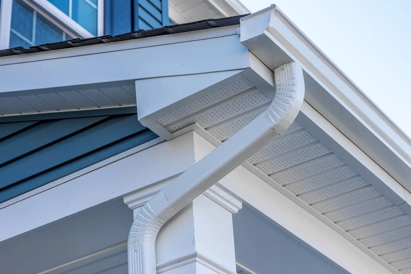 Soffit and fascia, perfectly aligned with a seamless white aluminum downspout that follows the vertical line of a white pillar against blue horizontal siding, demonstrating the high-caliber gutter services Illinois.