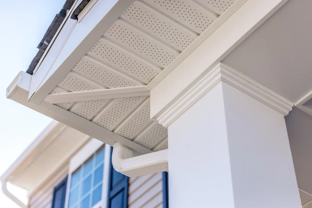 White perforated vinyl porch soffit ceiling with crown molding trim and a matching white downspout elbow.