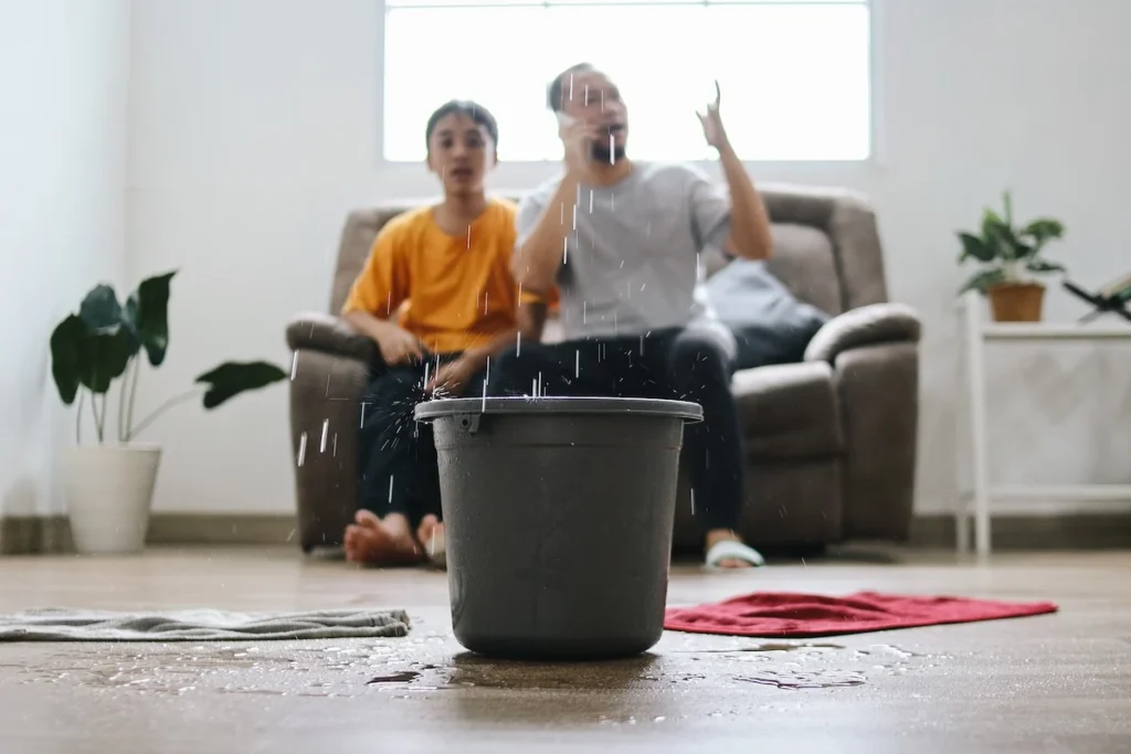 Water actively leaks from the ceiling, splashing into a black bucket placed on the floor.