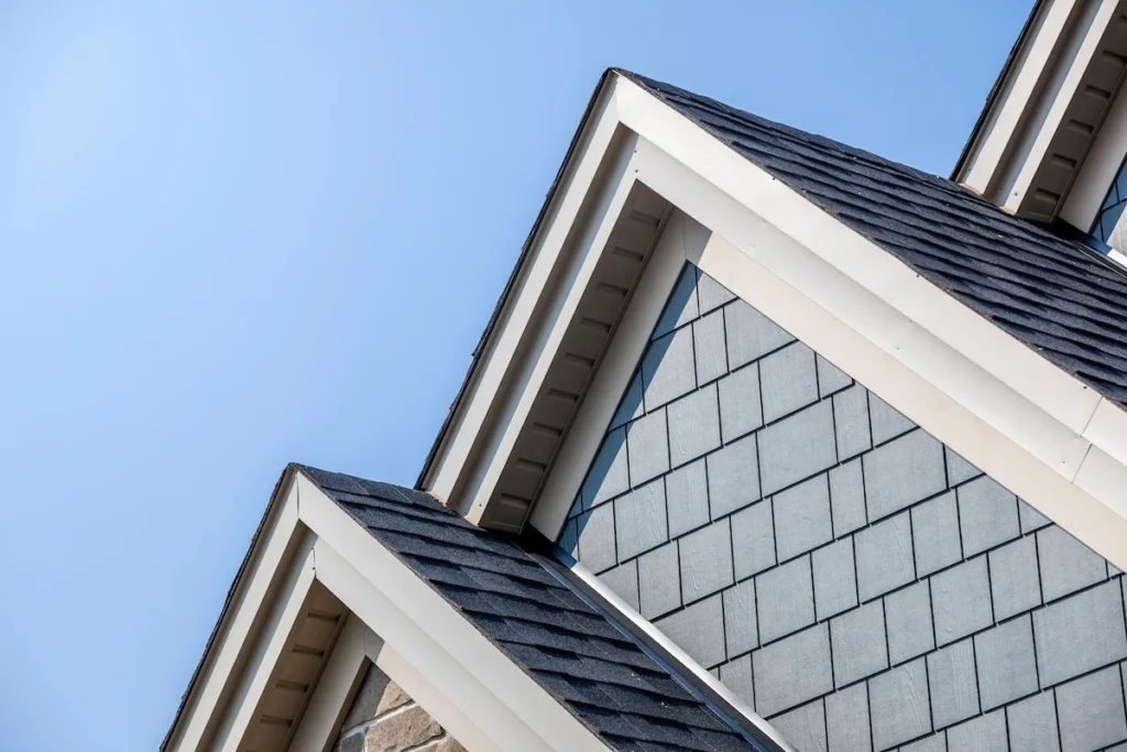Close-up of a house gable showing the vinyl soffit and fascia trim, dark asphalt roof shingles.