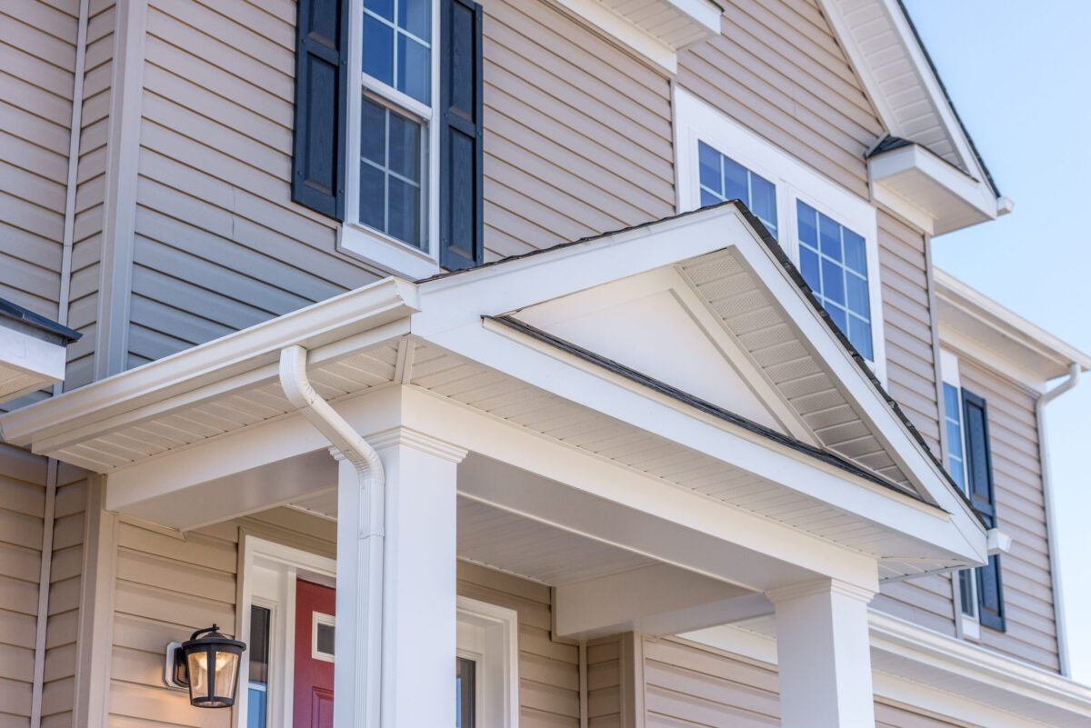 Portico leading to the entrance of vinyl horizontal lap siding covered building, with a roof structure over a walkway, supported by white rectangular columns on a new single family home in Maryland
