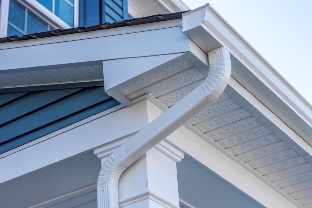 gutter installation Colonial white gutter guard system, fascia, drip edge, soffit providing ventilation to the attic, with pacific blue vinyl horizontal siding at a luxury American single family home neighborhood USA