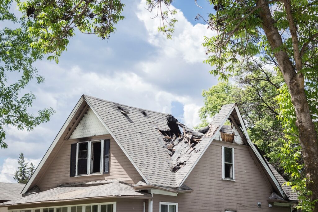 insurance roof replacement horizontal close up image of a roof of a house that has burned and fallen in under blue sky with cloud in summer time.