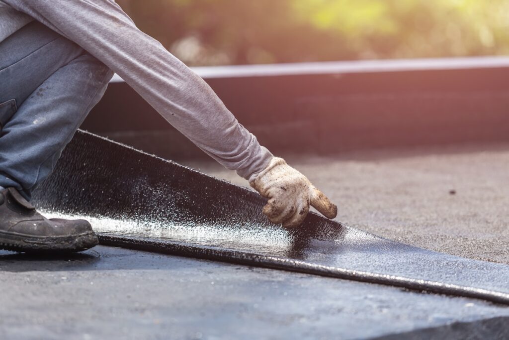 flat roof installation Asia worker installing tar foil on the rooftop of building. Waterproof system by gas and fire torching