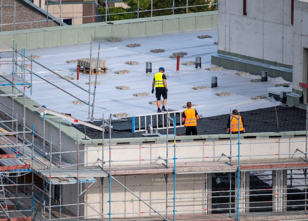 flat roof installation Birdseye view of roofer waterproofing the flat roof of a commercial building.